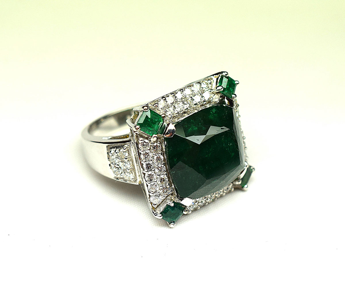 Important white gold ring set with 4 claws of a degree emerald probably Colombia weighing 16.59 c in a surround of modern round diamonds, enhanced at the 4 corners with square emeralds. Weight of the diamonds 1.50 c approx. G/VS quality. - Gold 16,19 g